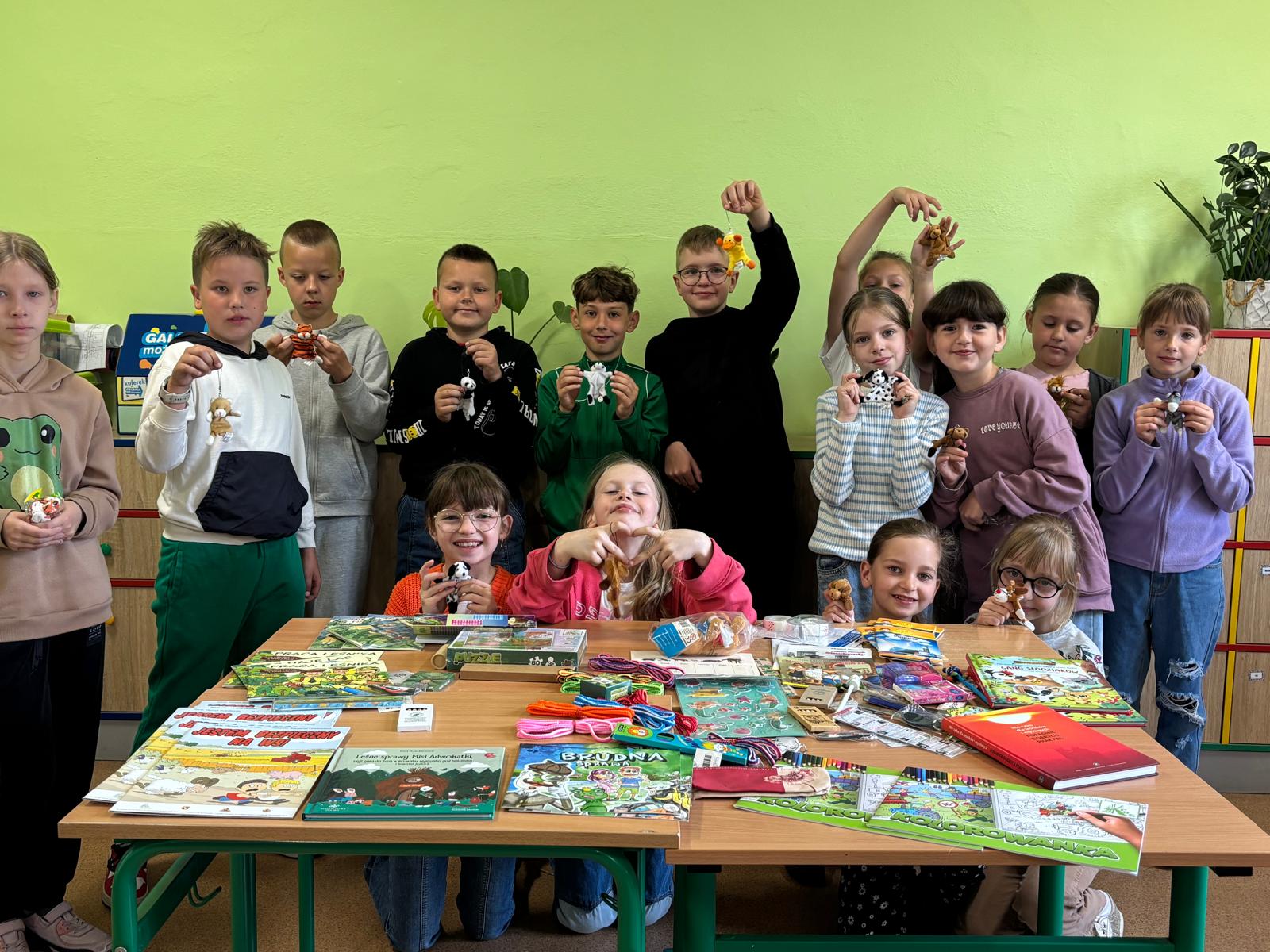 Zdjęcie grupy laureatów trzymających dyplomy przy stole z nagrodami